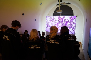 Uczniowie klasy policyjnej siedzący w grupie przez projektorem i oglądający film w sali muzeum.