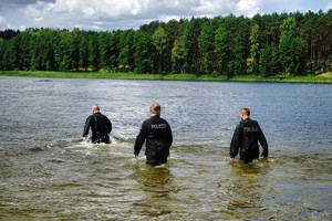 trzech policjantów wchodzi do wody w pełnym umundurowaniu