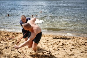 dwóch mężczyzn ciągnie linę i wyciąga z wody mężczyznę na brzeg