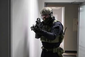 Uzbrojony policjant stoi przy ścianie trzymając w rękach długą broń