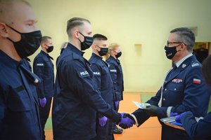 Sala gimnastyczna Oddziału Prewencji Policji w Łodzi, uroczystość ślubowania policjantów, komendant wojewódzki wręcza policjantowi legitymację służbową.