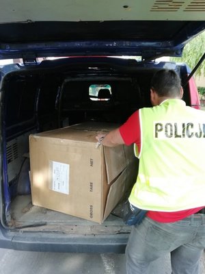 Mężczyzna w kamizelce odblaskowej z napisem policja stoi przed częścią bagażową auta w której widać duże pudło.