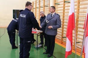 sala gimnastyczna Oddziału Prewencji Policji w Łodzi, uroczystość ślubowania nowo przyjętych policjantów, oficer wręcza legitymację służbową nowemu policjantowi