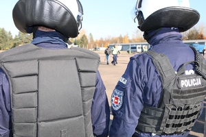 Policjanci w mundurach stoją plecami do obiektywu.