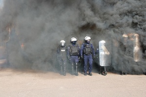 Policjanci z tarczami przechodzą przez dym.