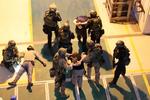 Wnętrze elektrowni, policjanci prowadzą zatrzymanych mężczyzn.