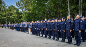 Kompania honorowa, mianowani i wyróżnieni policjanci, młodzi adepci stoją w szeregach, na końcu widać maszt flagowy i orkiestrę.