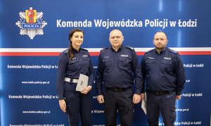 Policjanci stoją na ściance z aktami mianowania.