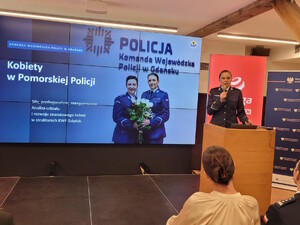 Policjantka za mównicą, mówi do mikrofonu, w tle prezentacja.