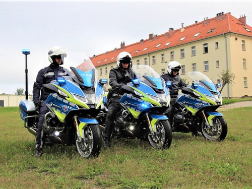 Trzy policyjne motocykle z policjantami ustawione w rzędzie, w tle budynek.