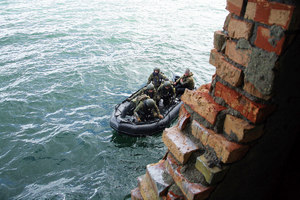 Policjanci na łodzi pontonowej podpływają do starego muru.