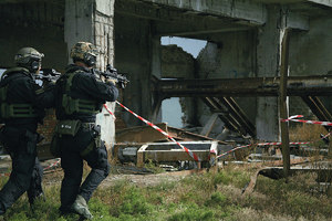Dwaj policjanci w umundurowaniu taktycznym i z bronią gotową do strzału idą wzdłuż ruin.