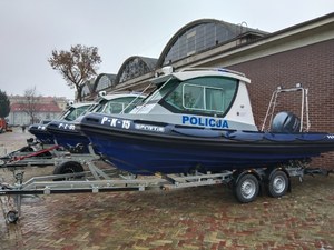 Kilka policyjnych łodzi na przyczepach do transportu ustawionych w szeregu. Na burcie pierwszej napis P-K-15.