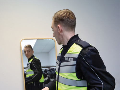 Policjant ruchu drogowego przymierza nowy kombinezon motocyklowy, przegląda się w lustrze.