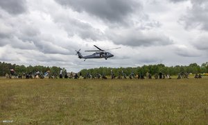 Zdjęcie przedstawia lądujący na polanie śmigłowiec typu Black Hawk.
Niebo nad polaną jest zachmurzone, a w tle widać drzewa oraz ludzi uczestniczących w szkoleniu.