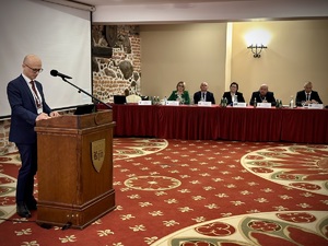 Zdjęcie przedstawia jednego z prowadzących konferencję ubranego w ciemny garnitur i białą koszulę. W centralnej części zdjęcia znajduje się stół prezydialny, przy którym siedzią przedstawiciele dyrekcji i kierownictwa Policji.

Za plecami prowadzącego znajduje się wyświetlacz, który jest wyłączony.