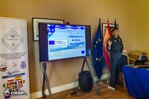 Zdjęcie przedstawia przedstawiciela hiszpańskiej policji, który prowadzi szkolenie, za jego plecami znajdują się trzy flagi: dwie unii europejskiej oraz - w środku - hiszpańska.

Po lewej stronie znajdującego się w środkowej części obrazka ekranu widać roll-up promocyjny projektu &quot;EMERALD&quot;