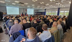 Zdjęcie przedstawia uczestników szkolenia, którzy siedzą na sali. Uczestnicy obserwują prelegenta oraz dwa ekrany, na których wyświetlane są informacje dot. tematu szkolenia.