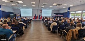 Zdjęcie przedstawia uczestników szkolenia, którzy siedzą na sali. Uczestnicy obserwują prelegenta oraz dwa ekrany, na których wyświetlane są informacje dot. tematu szkolenia.