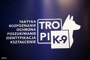 Obraz przedstawia logo projektu TROPIK-9: element graficzny przedstawiający zarys sylwetki psa wraz z dwoma nachodzącymi na siebie kwadratami: w jeden wpisany został biały napis: TROPI na niebieskim tle, w drugi - niebieski napis K-9 na białym tle.

Obok elementu graficznego, uszeregowane w sześciu wersach, znajdują się napisy składające się na rozwinięcie akronimu projektu: Taktyka, Rozpoznanie, Ochrona, Poszukiwanie, Identyfikacja, Kształcenie.