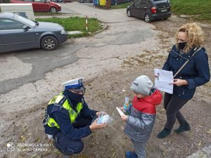 Policjant sochaczewskiej drogówki przekazuje maseczkę ochronna dziecku i jego mamie