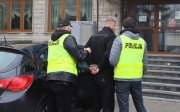 Policjanci ubrani w kamizelki odblaskowe prowadzą zatrzymanego mężczyznę