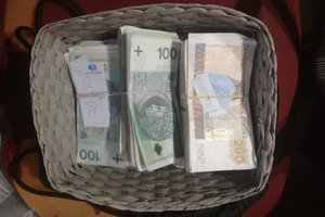 Pliki banknotów o nominałach 100 i 200 PLN leżące w koszyku.