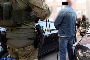 Dwaj policjanci stojący z zatrzymanym mężczyzną obok samochodu.