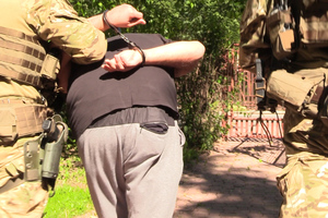 Funkcjonariusze prowadzą zatrzymanego mężczyznę  w kajdankach zapiętych z tyłu.