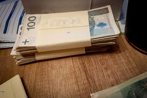 Dwa pliki banknotów o nominale 100 PLN, leżące na blacie stołu.