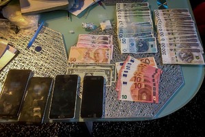 Leżące na stole banknoty polskie oraz zagraniczne. Obok 4 telefony komórkowe i srebrne foliowe zawiniątko.