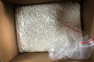 Plastikowa torba leżąca wewnątrz kartony, wypełniona tysiącami sztuk tabletek.