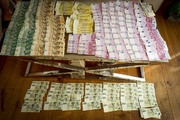 Kilkaset banknotów w różnych walutach i nominałach leżących na stole oraz na podłodze.