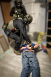 Policjanci podnoszą zatrzymanego mężczyznę leżącego na podłodze.