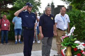 Fotografia kolorowa na której widać umundurowanego policjanta oraz dwóch mężczyzn. Policjant oraz mężczyźni oddają hołd nad grobem zmarłemu Generałowi Markowi Papale.