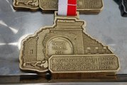 medal w kształcie muru z brama z napisem Twierdza Przemyśl 2021, poniżej napis V Mistrzostwa Polski Służb Mundurowych w Siatkówce Plażowej Przemyśl 21-22.08.2021 r.