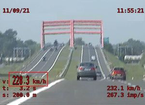 Stopklatka z nagrania z policyjnego wideorejestratora. W czerwonym prostokącie zaznaczona prędkość rejestrowanego bmw. W górnym lewym rogu - data, w górnym prawym rogu - godzina