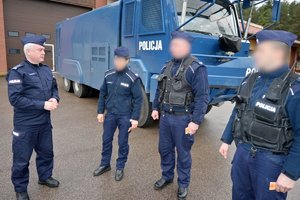 Po lewej Komendant Wojewódzki Policji w Rzeszowie, po prawej trójka policjantów stojących obok siebie w odstępach. Za nimi w tle policyjna ciężarówka.