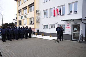 przemawiający na tle komisariatu Komendant Wojewódzki Policji, z lewej strony policjanci w szyku