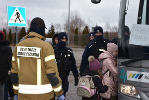 Policjanci i strażak przy autobusie do którego wsiadają dzieci