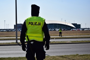Policjant oddziału prewencji stoi przy ulicy. W tle terminal lotniska Rzeszów-Jasionka.