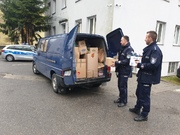 dwóch policjantów wkłada zebrane przedmioty do policyjnego samochodu