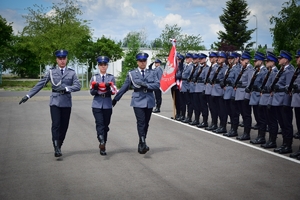 Poczet flagowy (trójka policjantów - w środku policjantka trzymająca w rękach złożoną flagę), w tle kompania honorowa.