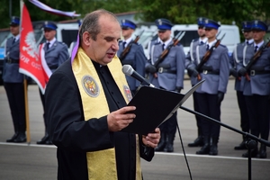 Duszpasterz Podkarpackiej Policji przy mikrofonie, dalej w tle zaproszeni goście i kadra kierownicza KWP.