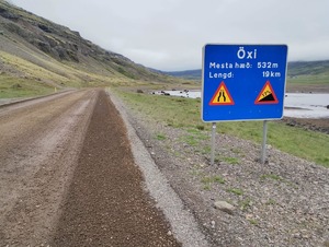 znak drogowy, stojący przy drodze przedstawiający trudny teren