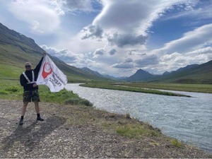 mężczyzna stojący z flagą na tle gór i jeziora