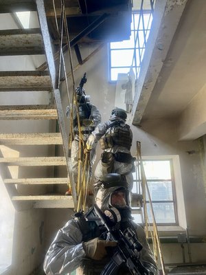 mundurowani policyjni kontrterroryści  w szyku bojowym, z bronią sprawdzają pomieszczenia wewnątrz budynku