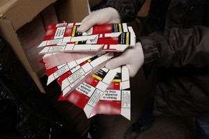 Policjant w białych rękawiczkach pokazuje kartoniki, z których produkowane były opakowania do papierosów