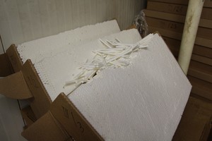 Na zdjęciu widać trzy otwarte kartony z białymi filtrami do produkcji papierosów, kartony są oparte o ścianę