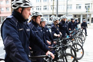 policjanci w mundurach i kaskach na głowach stoją na ulicy z rowerami poolicyjnymi